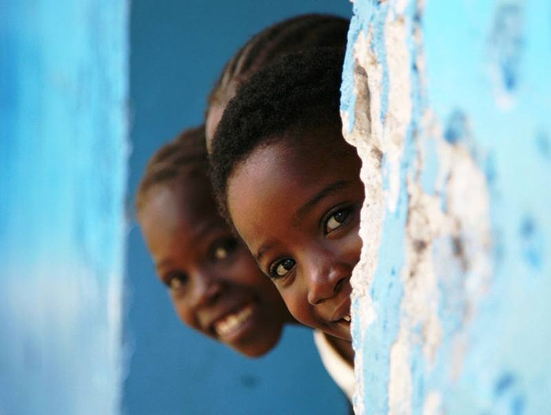 four young children in a developing country dressed in matching red and white clothes smiling and laughing