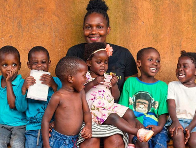 a woman and 6 young children posing while laughing and smiling in a developing country