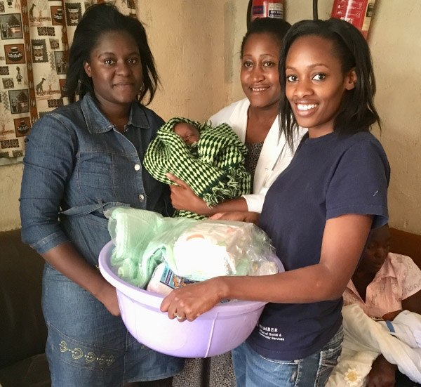 three women together with one holding an infant and another holding a container of baby supplies
