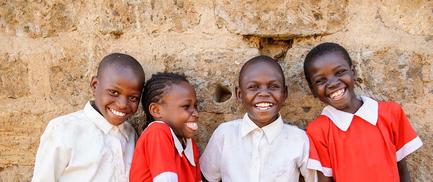 four young children in a developing country dressed in matching red and white clothes smiling and laughing