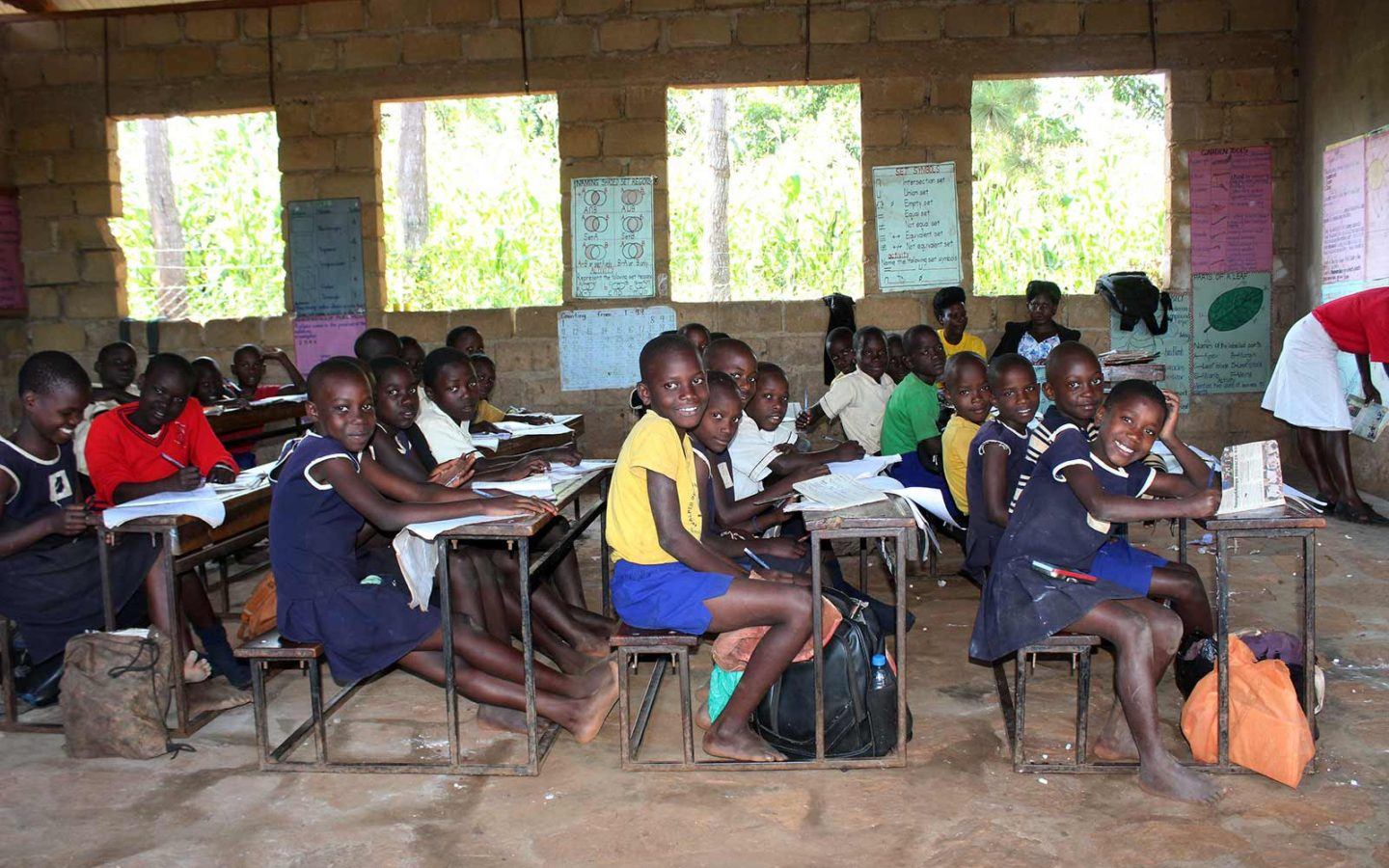 a classroom full of smiling children sitting at their desks in a developing country