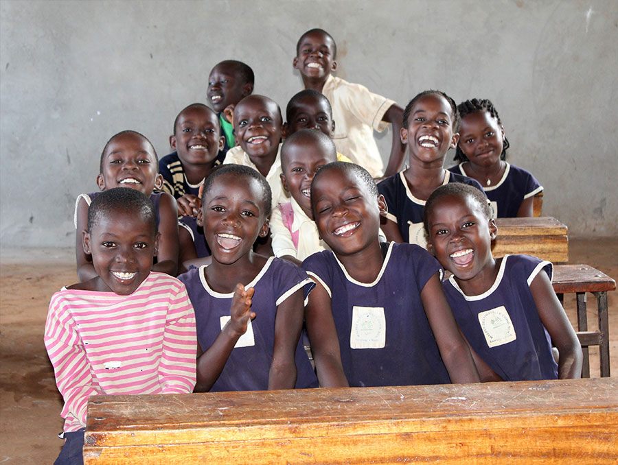 a group of school-age children in a developing country classroom sitting together at a desk and smiling