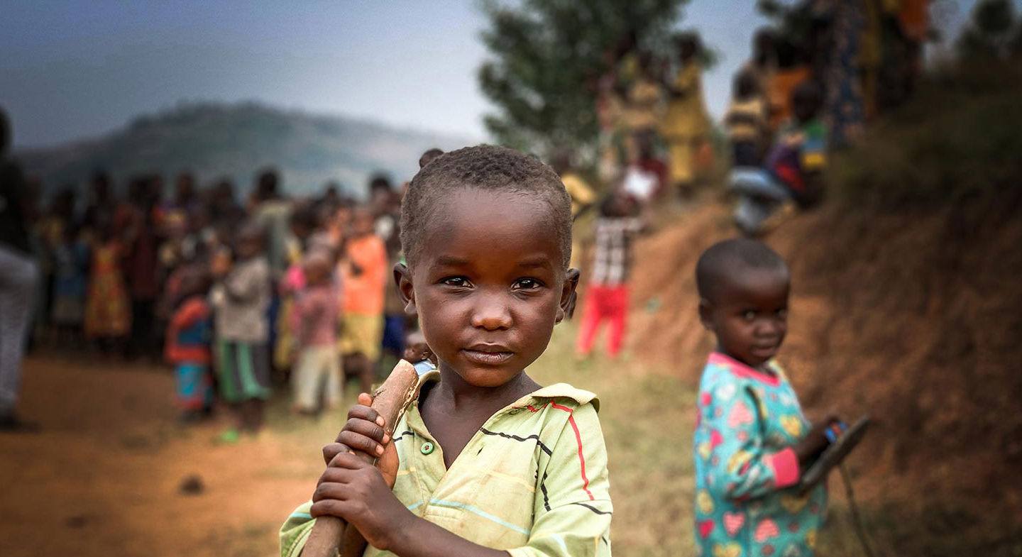 a young boy holding a tree branch like a walking stick outdoors in Kenya