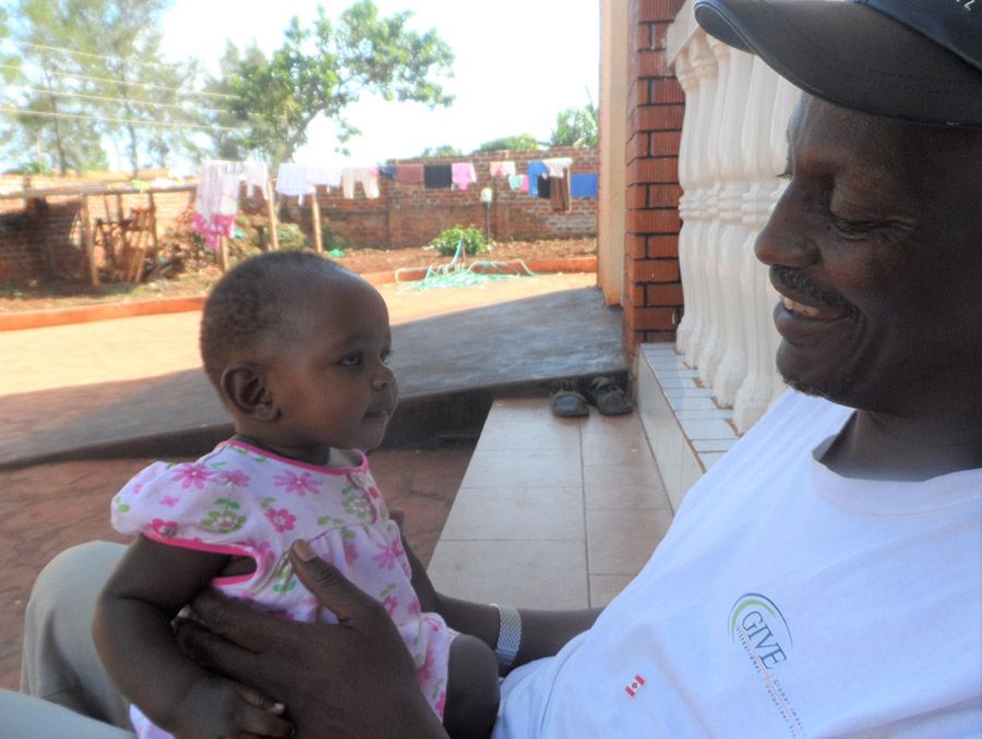 Farouk Matovu smiling and holding a baby